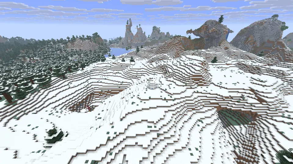 Small white igloo on rolling snowy hills beside a rocky hollow, with spruce forest and peaks behind