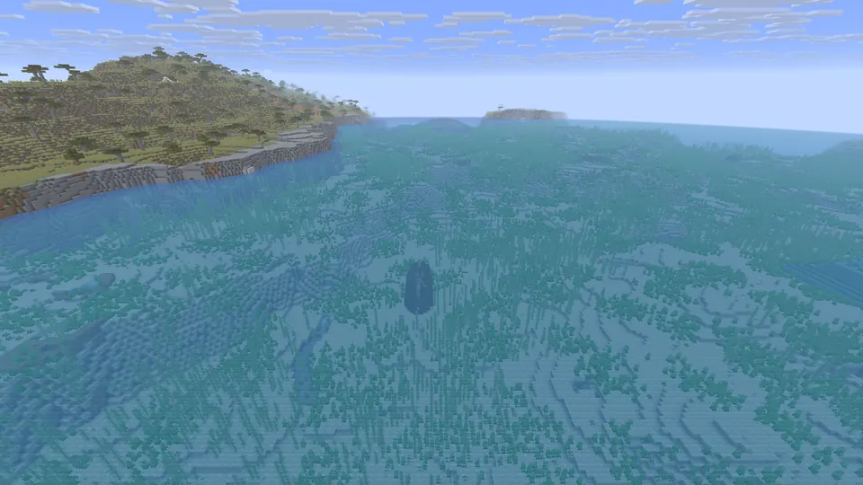 Clear sea with a dark ship-shaped shadow on the bottom and a savanna headland on the left
