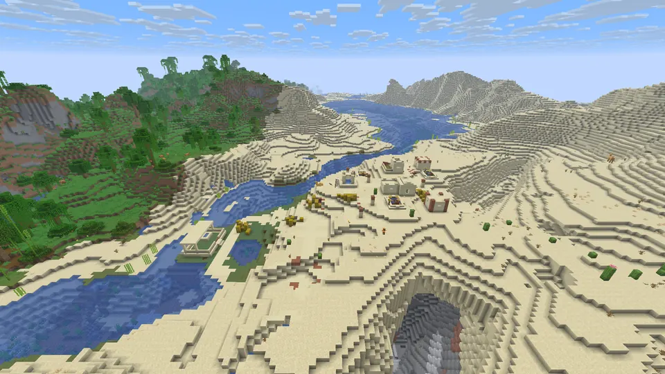 Sandstone village houses beside a river winding between sand dunes, with jungle hills on the left